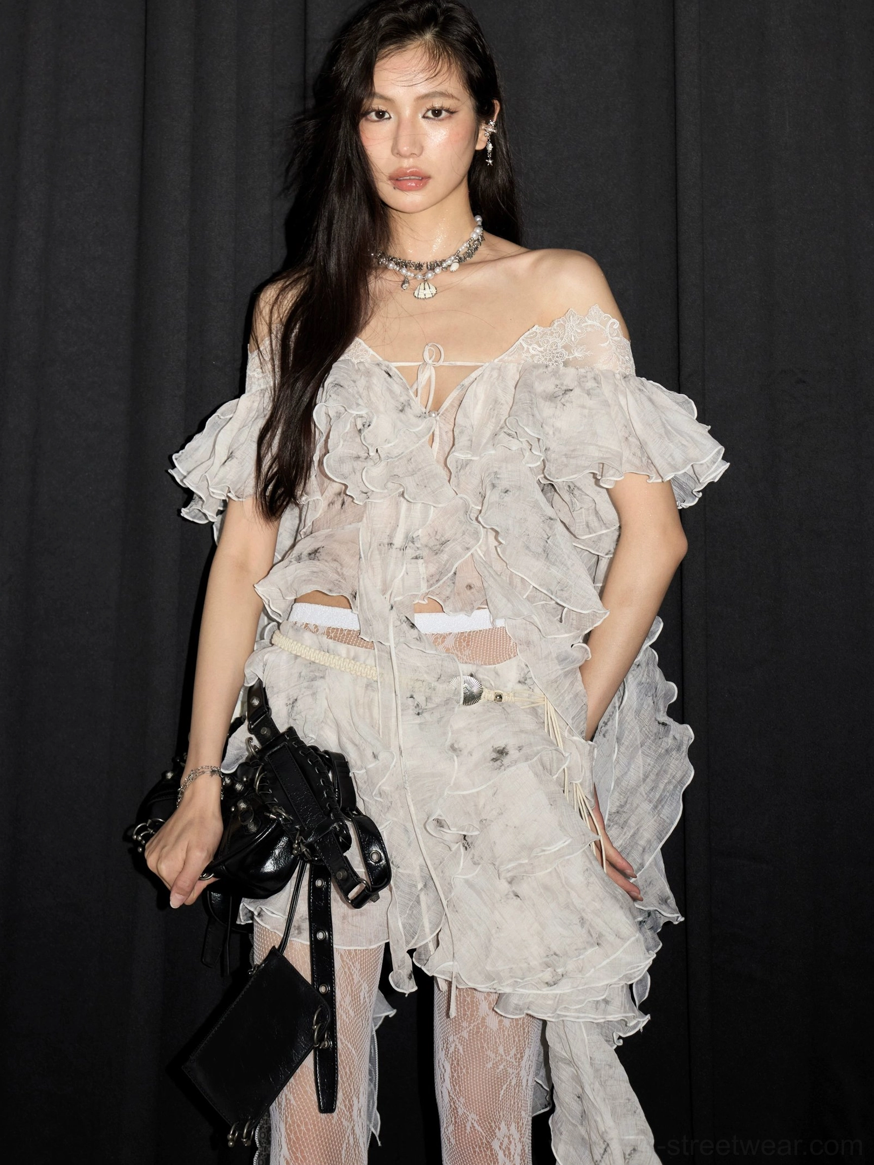 Close front view of a white distressed lace ruffle two-piece set with lace-up off-shoulder neckline, cropped cutout and black crossbody bag