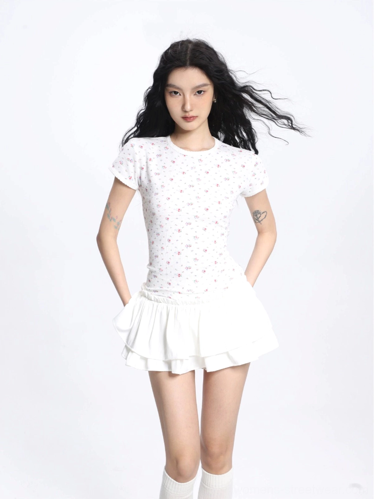 Front view of a white double layer ruffled mini skirt with a tailored high waist, styled with a cropped floral top and over the knee socks