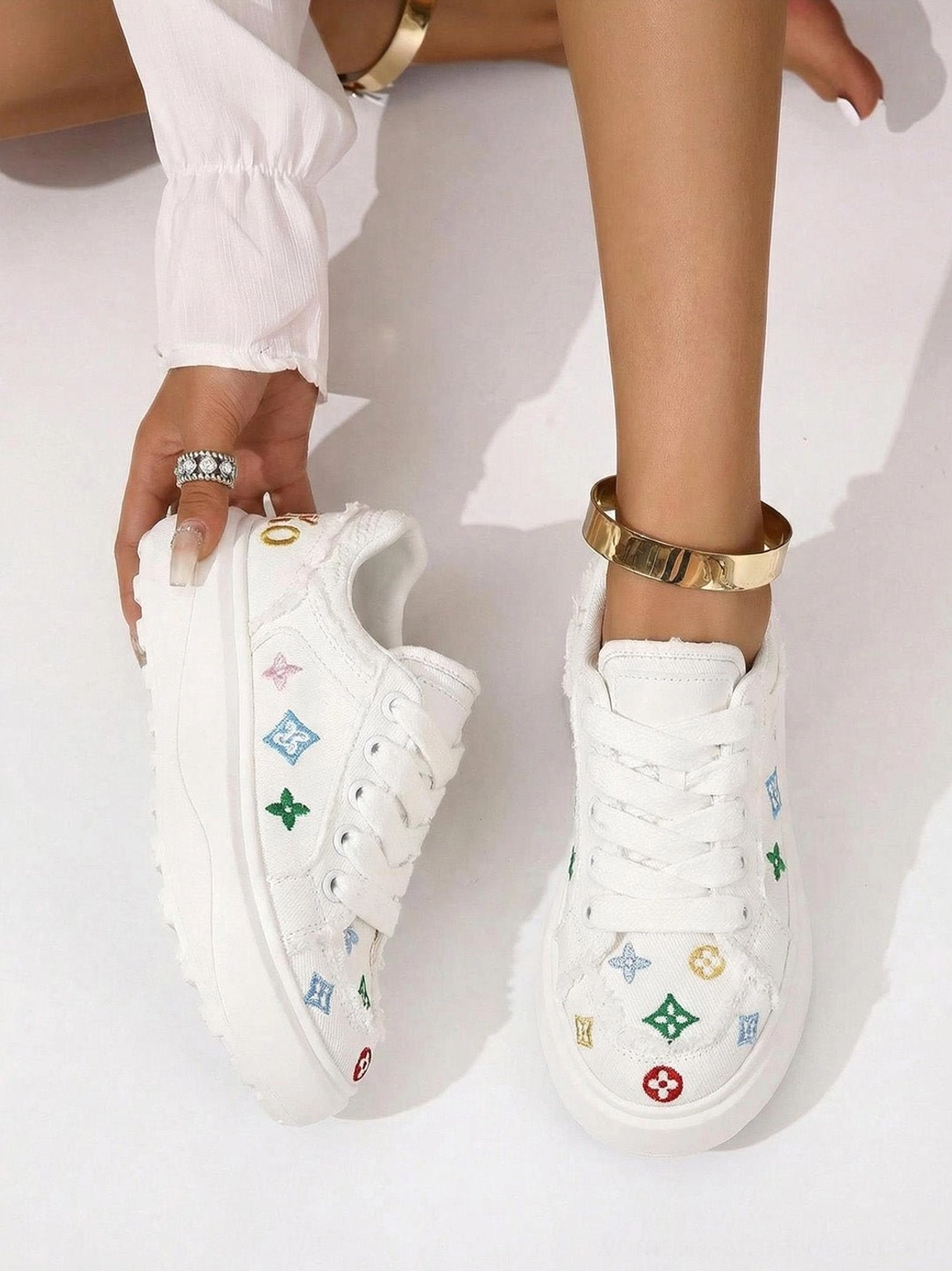 Close-up of white embossed platform skate sneakers held by model showing frayed trim colorful motifs and platform construction