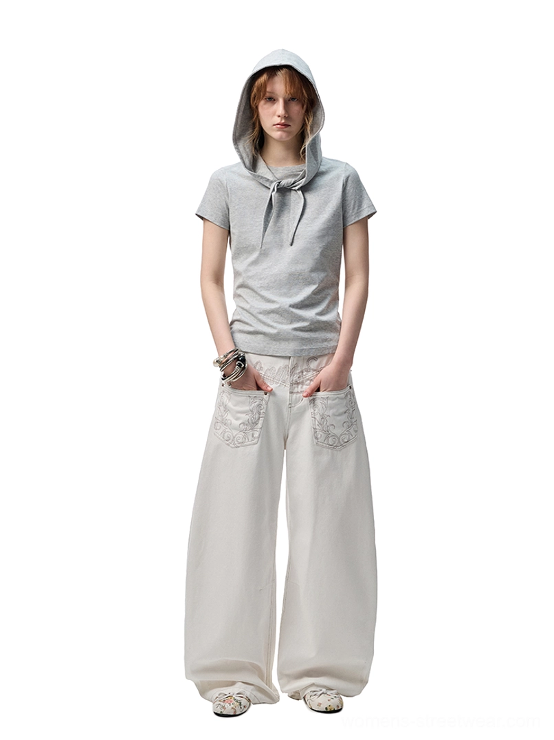 Female model styling white embroidered wide-leg jeans with a cropped gray hooded tee for a clean modern streetwear look