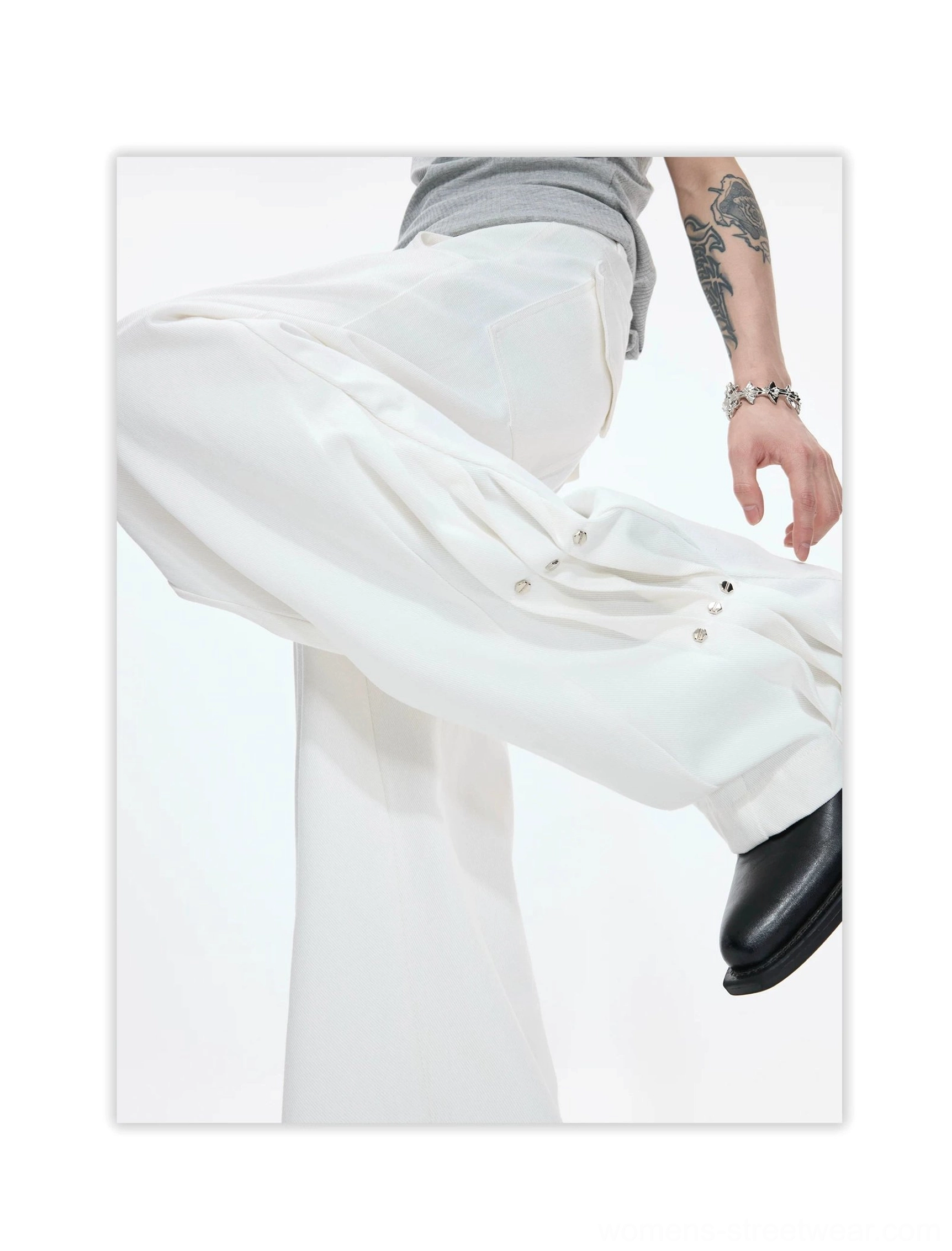 White extra-wide-leg avant-garde streetwear pants shown in motion with pleated front, adjustable side snap fasteners, metal rivets, and fluid cotton drape