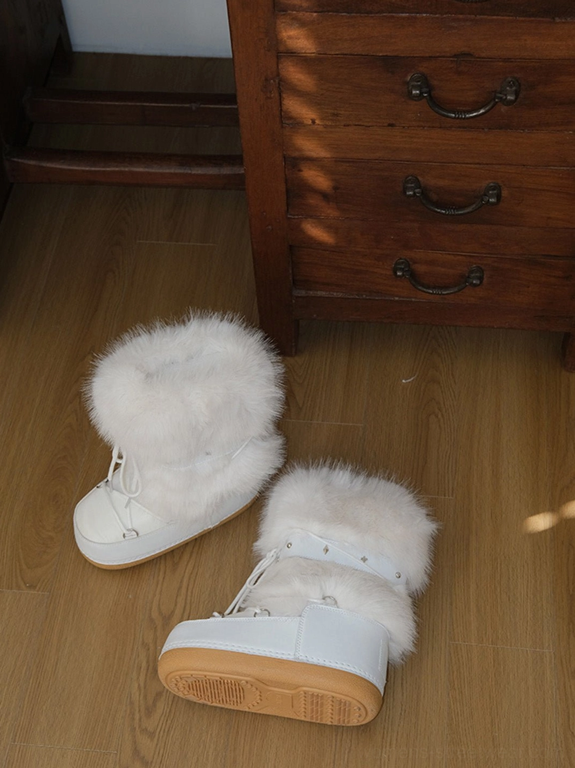 Overhead side view of white lace-up faux fur snow boots showing plush fur cuffs and thick rubber platform outsoles