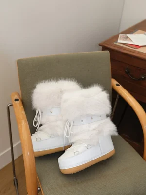Pair of white faux fur snow boots with platform soles displayed beside a wooden chair in a cozy indoor setting