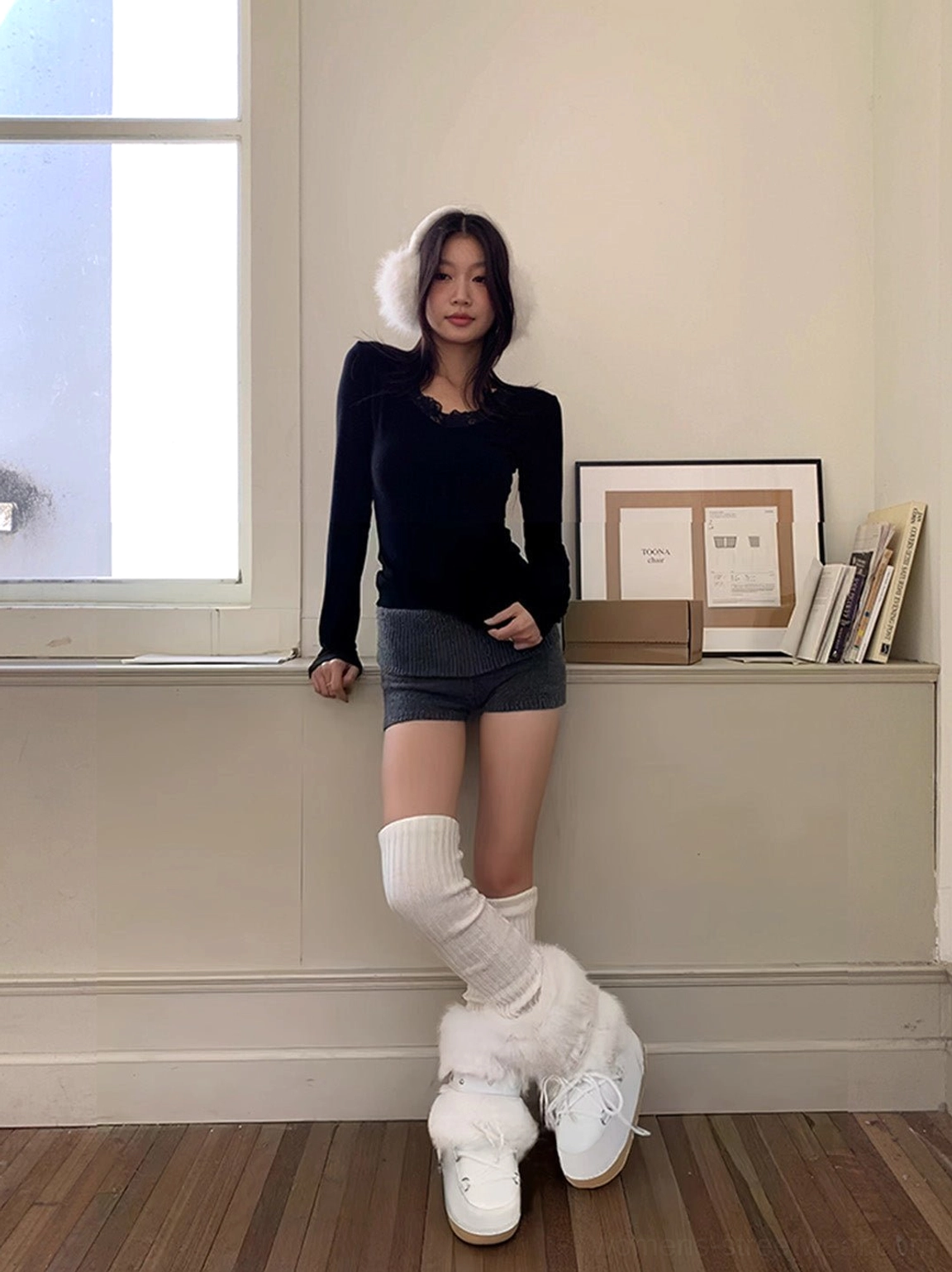 Model wearing white faux fur platform snow boots with over-the-knee knit socks, denim shorts, and a black long-sleeve top