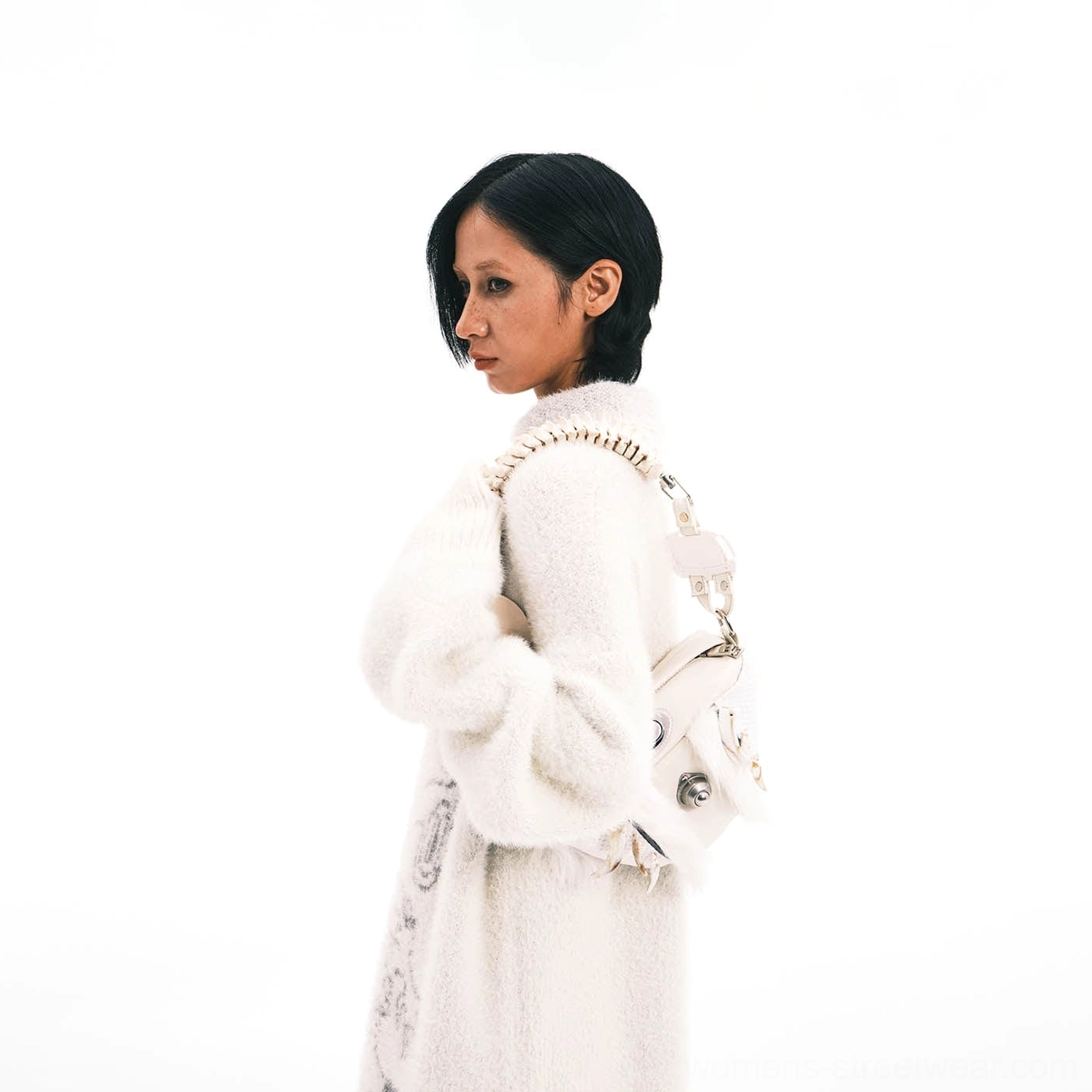 Female model styling white faux fur skeletal spine handle shoulder bag over a soft white fuzzy knit outfit