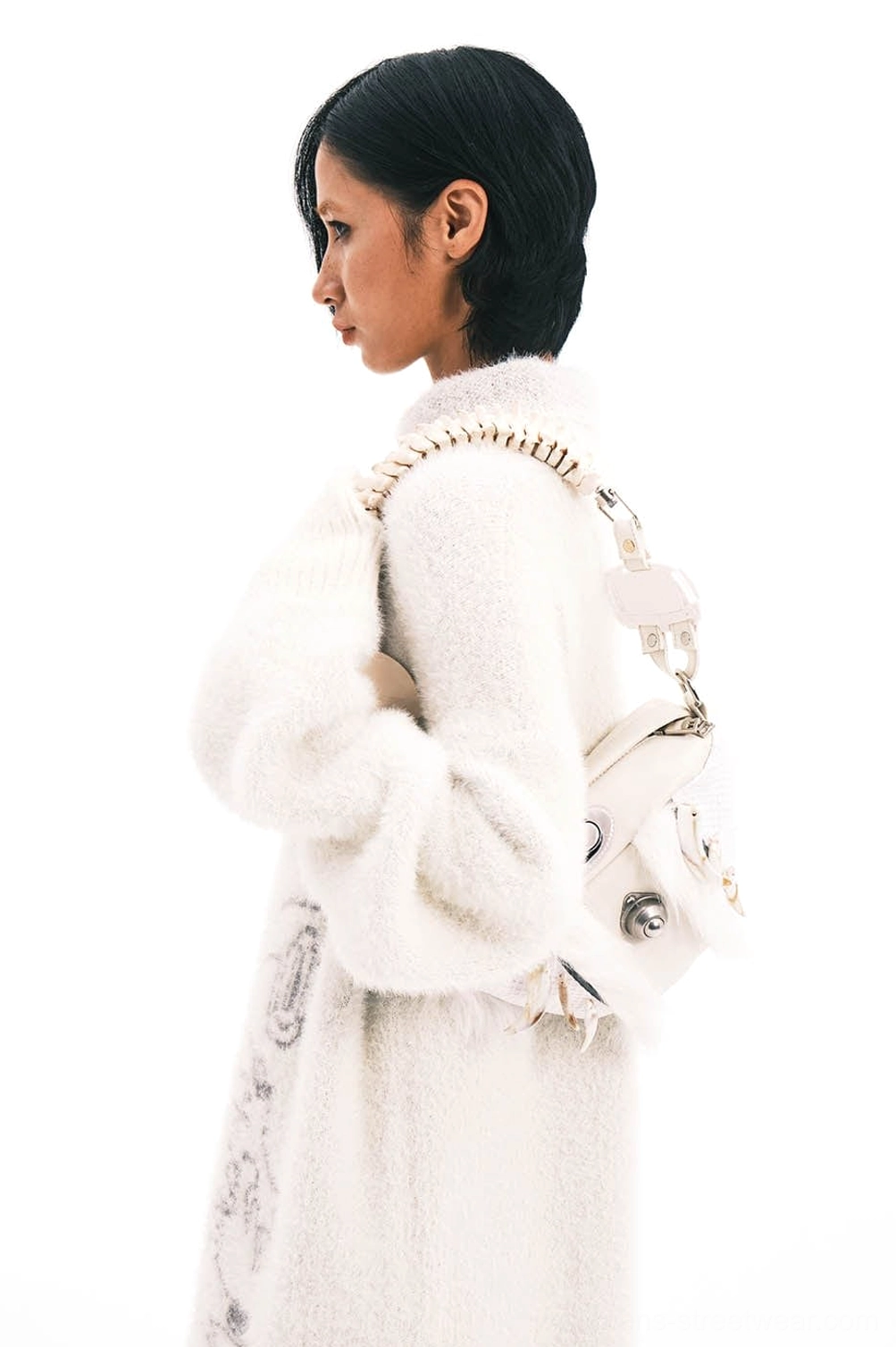 Side view of white faux fur skeletal spine handle shoulder bag worn over a white textured knit coat