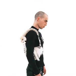 Male model wearing white faux fur skeletal spine handle shoulder bag as a crossbody with black streetwear outfit
