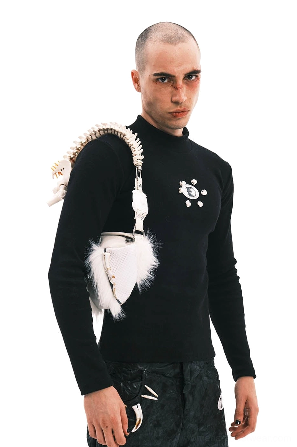 Male model wearing white faux fur skeletal spine handle shoulder bag at the hip with black tactical streetwear