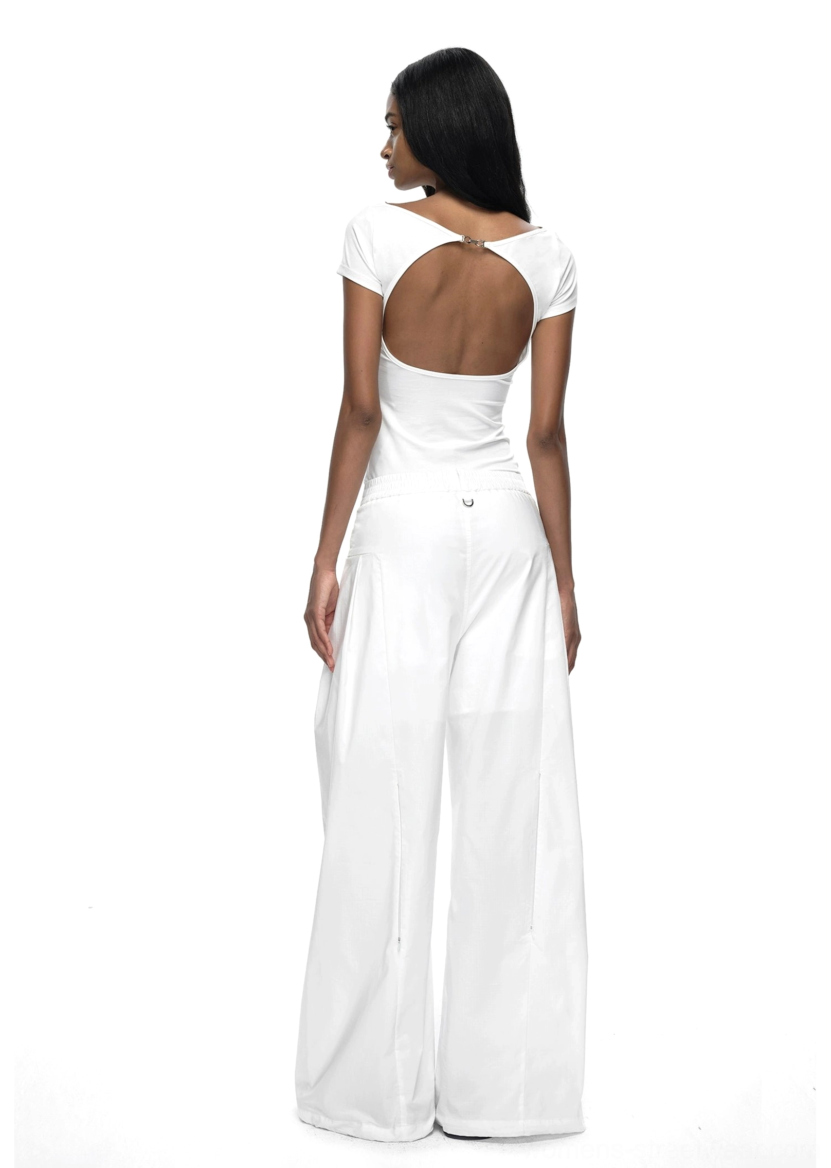 White fitted backless short-sleeve streetwear T-shirt showing the large open-back design with white trousers