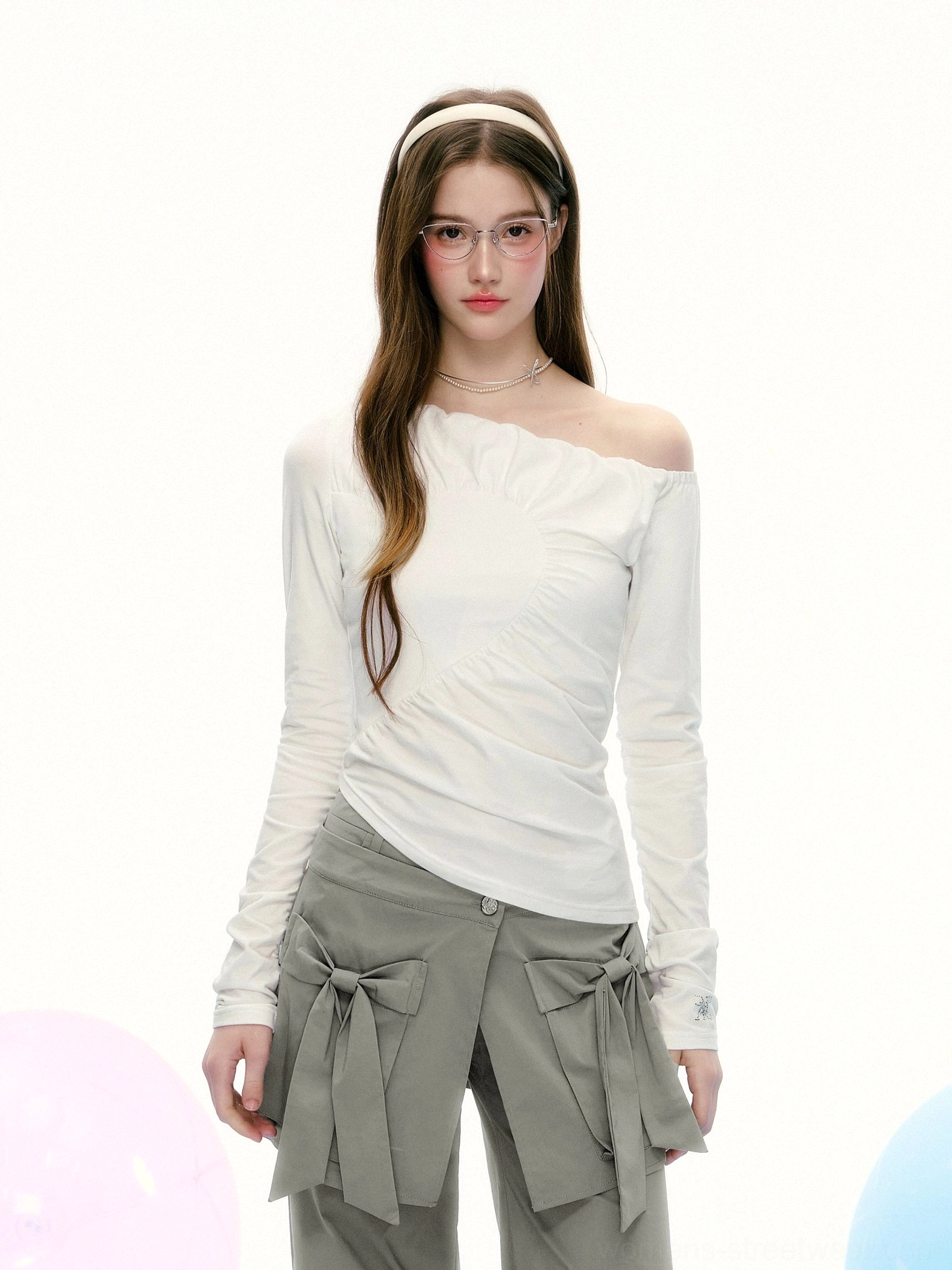 Half-body view of a fitted white off-shoulder asymmetrical top featuring a slanted ruched front and modern avant-garde streetwear silhouette