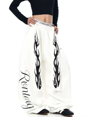 White oversized wide-leg fleece sweatpants with black flame graphics and cursive script detail styled with a cropped black top
