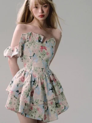 Three-quarter back view of a white floral ruffle mini dress featuring an off-shoulder silhouette, fitted corset bodice, flared skirt, and layered ruffle sleeves