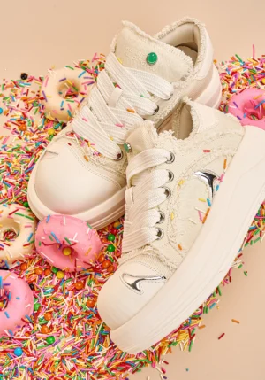 Top view of white frayed canvas platform skate sneakers with wide flat laces, green heel tabs, and metallic accents