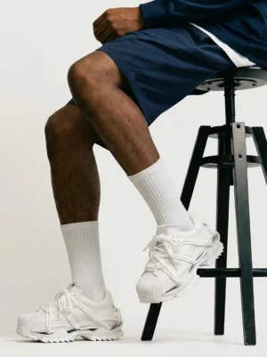 White futuristic chunky runner sneakers styled with navy shorts and white crew socks in a low front streetwear view, highlighting the chunky runner sole and technical layered upper