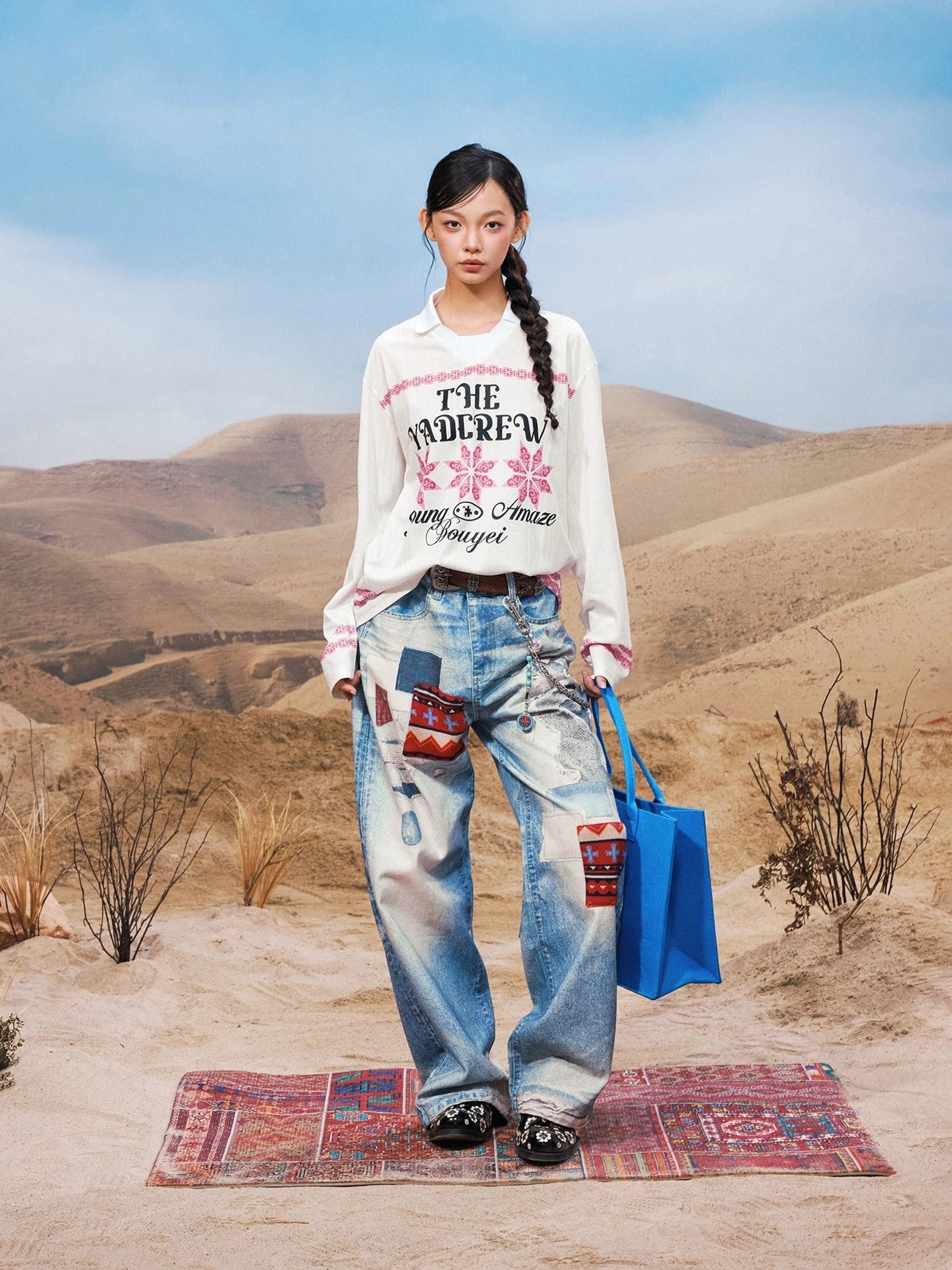 White oversized geometric graphic polo collar long sleeve streetwear shirt with pink snowflake motifs shown from the front with a blue tote bag