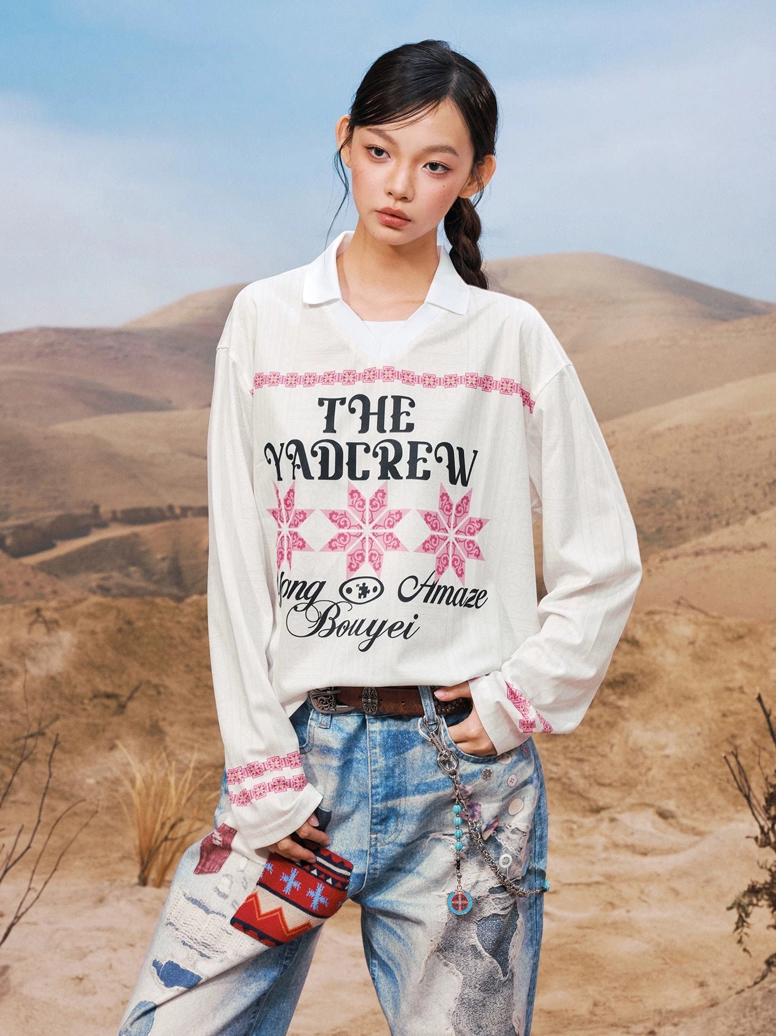 White geometric graphic collared long sleeve streetwear shirt shown from the front three-quarter view with pink ethnic-inspired motifs and ripped jeans