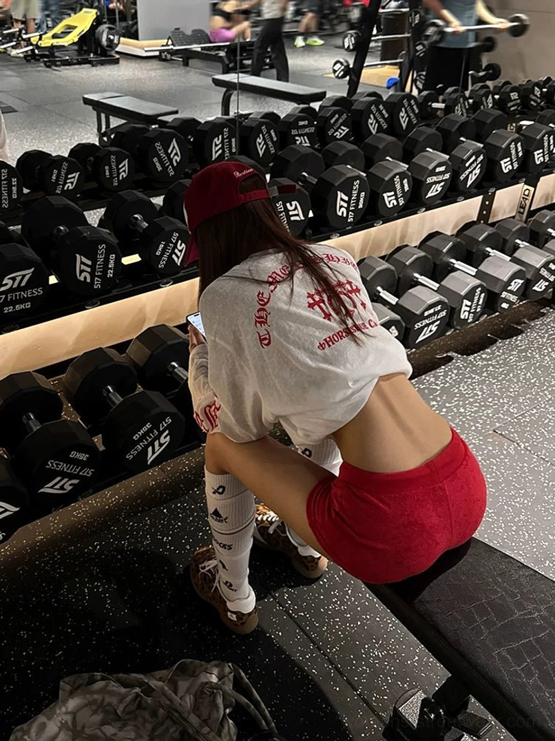 Back view of a loose white gothic graphic long-sleeve tee with bold red sleeve prints styled with fitted red athletic shorts
