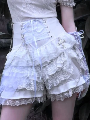 Close-up front view of white Gothic Lolita lace ruffle shorts with high waist lace-up detail, layered frills, cross pendants, and chain accents
