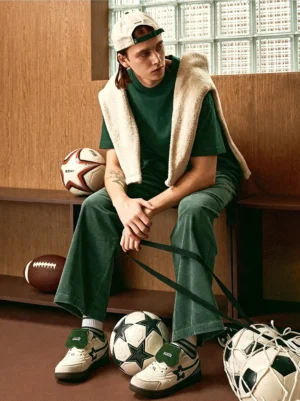 Male model wearing white and green detachable tongue streetwear sneakers with a retro green sports outfit and shearling coat