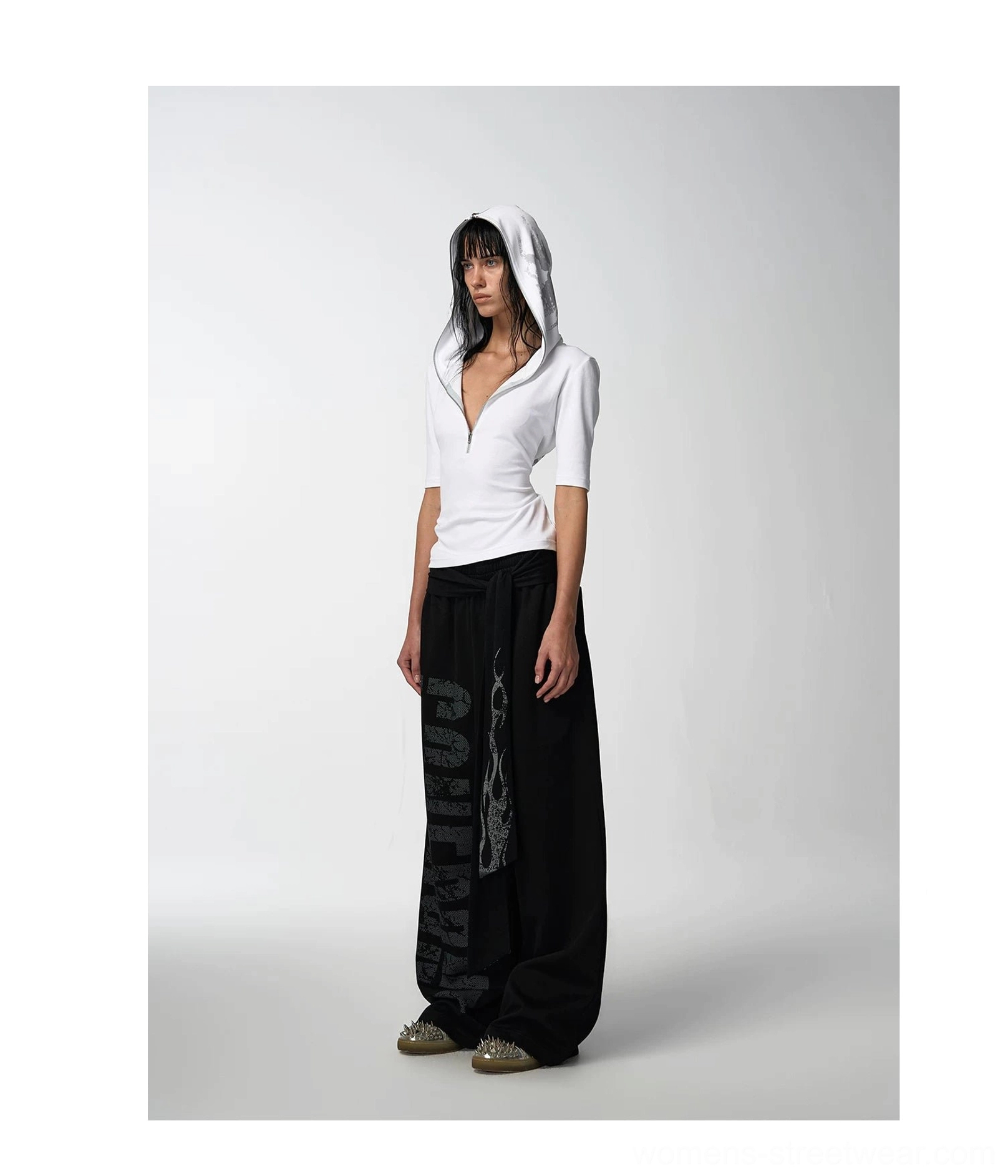 Front view of a white half-zip hooded graphic streetwear tee styled with black flame-print wide-leg trousers