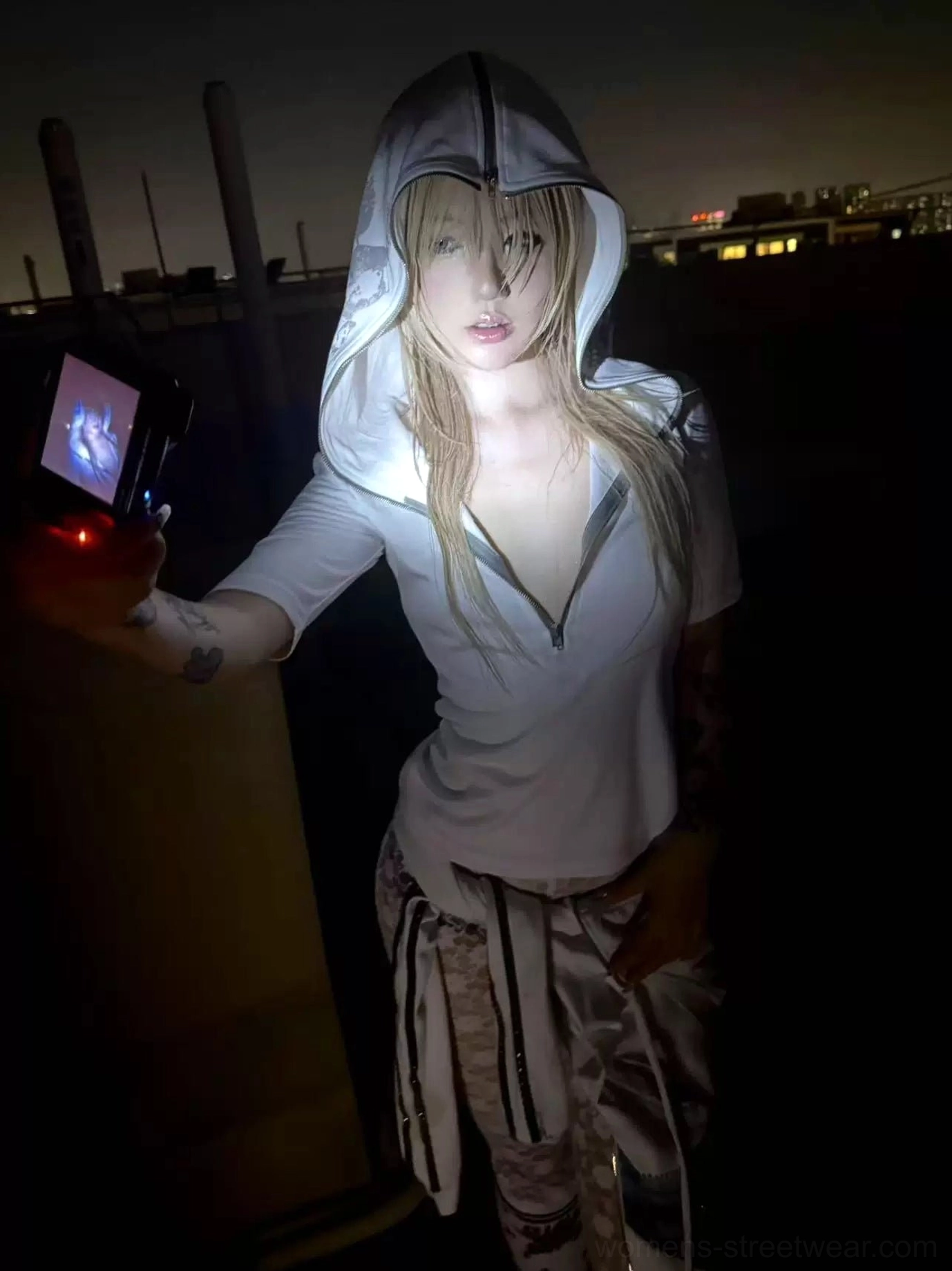 Close full-body view of a fitted white half-zip hooded streetwear top styled with striped wide-leg pants at night