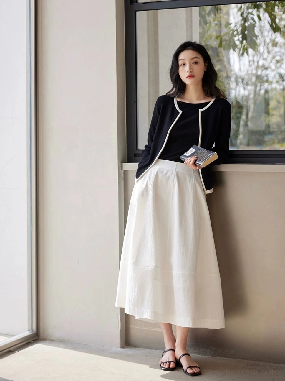 White high waist A-line maxi skirt paired with a black contrast trim knit cardigan in a bright window studio