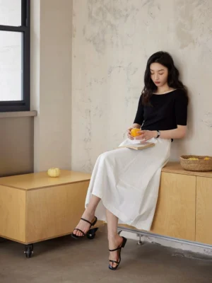 White high waist flowing maxi skirt with fitted black boat neck top in a relaxed seated Korean minimalist fashion look