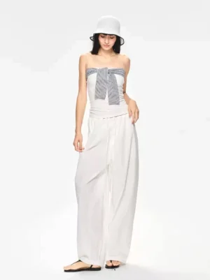 Front view of white high-waisted draped wide-leg streetwear pants styled with a strapless bow camisole and white bucket hat