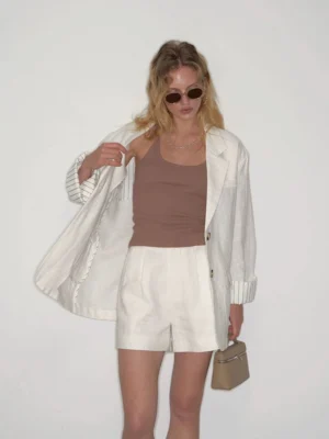 Close-up view of white high-waisted pleated linen shorts styled with a matching linen blazer and beige mini handbag for a tailored Korean fashion outfit