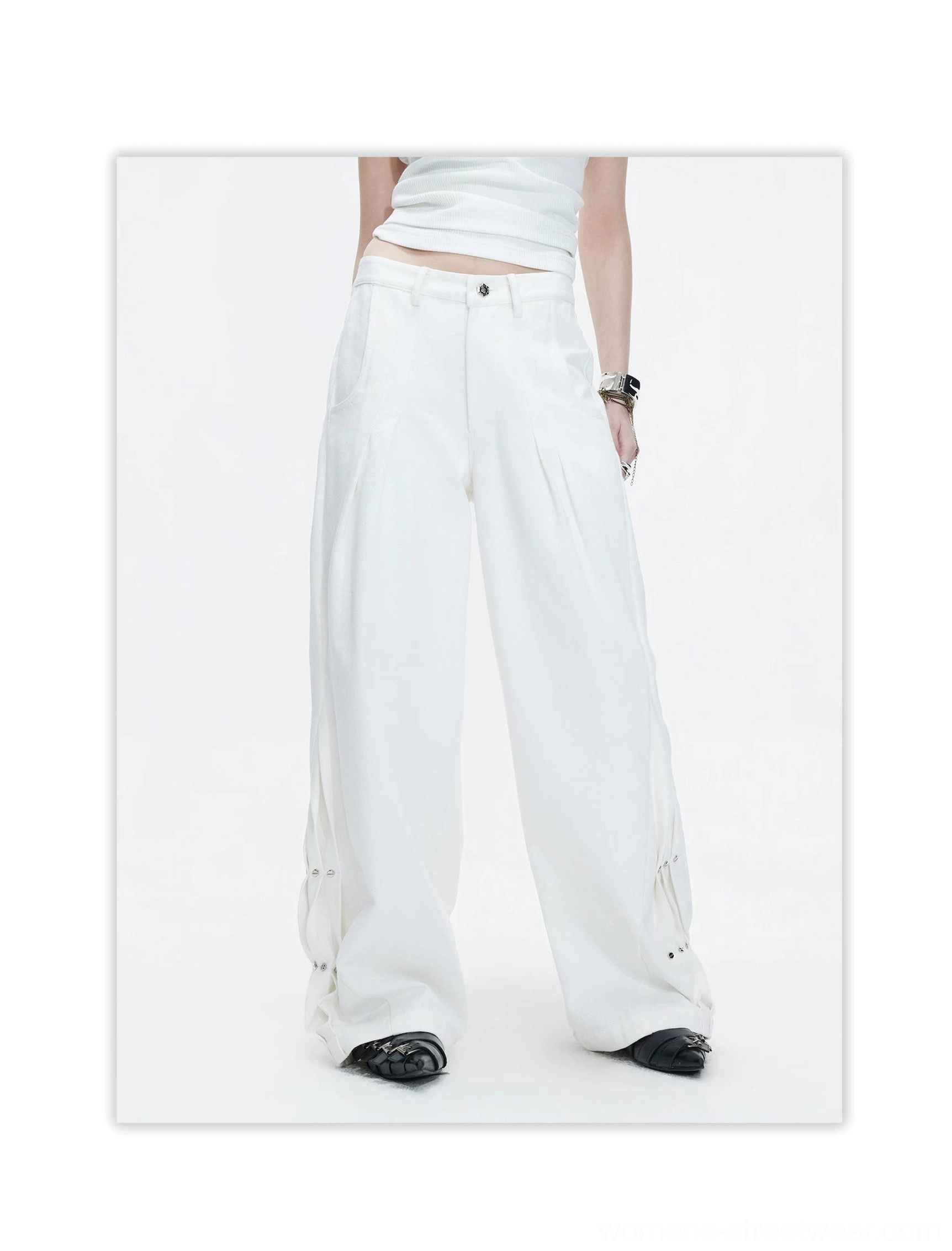 Full-body front view of white high-waisted wide-leg streetwear pants with front pleats, smooth woven cotton fabric, lower-leg rivets, and dramatic draped proportions
