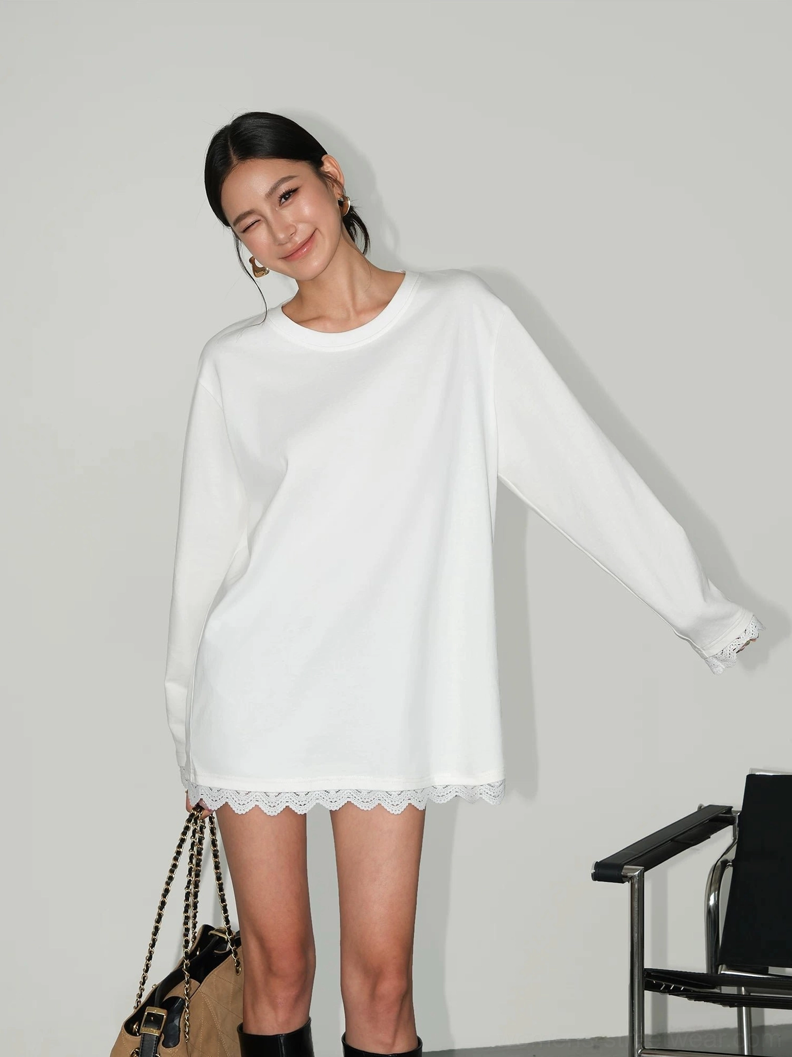 White oversized lace-hem long-sleeve tee dress styled with black knee-high boots and a two-tone handbag in a three-quarter view
