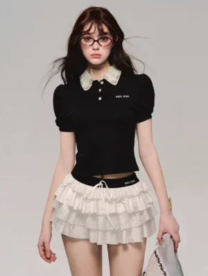 White lace tiered mini skirt with black polo top two-piece set worn by female model with glasses, studio fashion photography full-body front view
