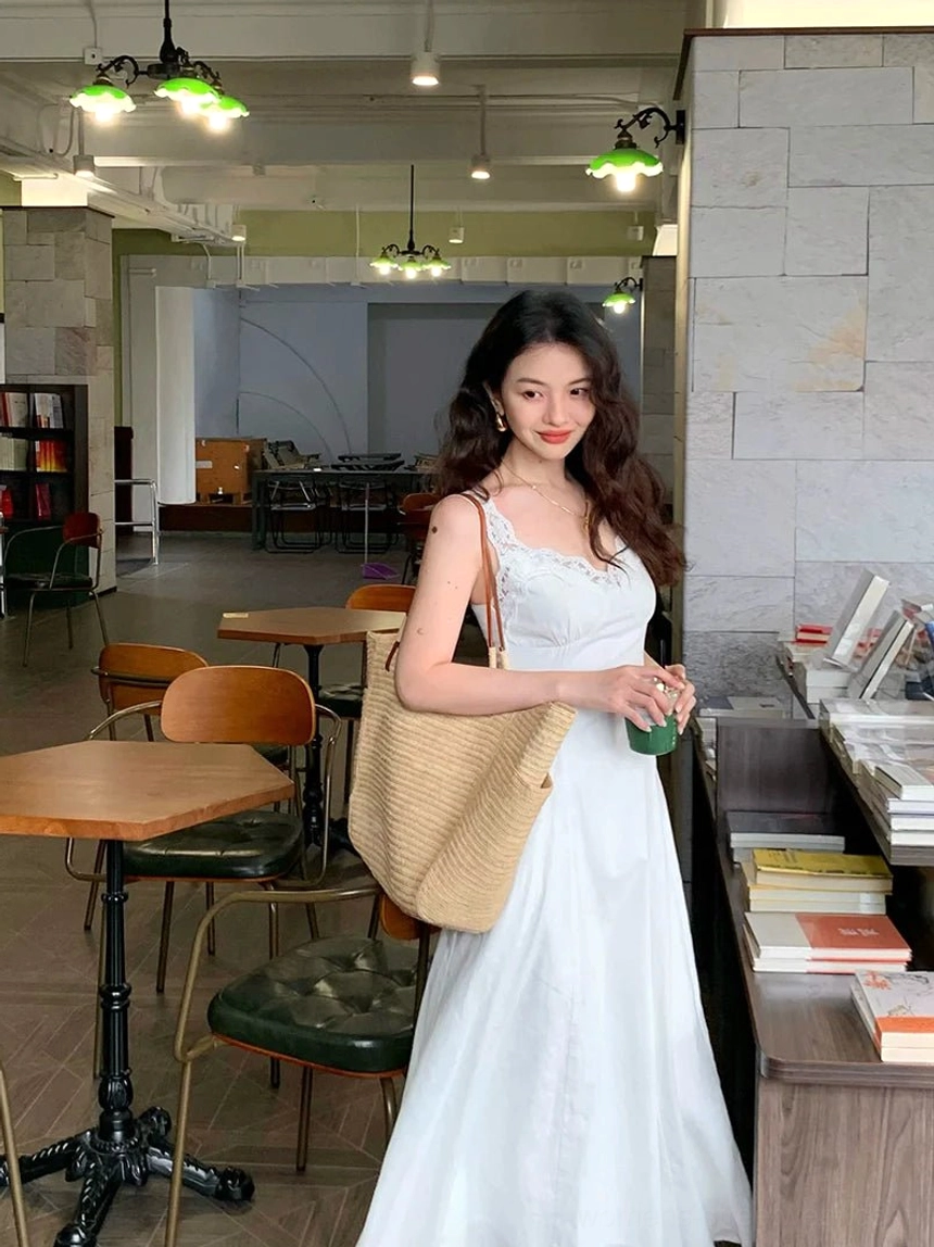 White lace trim linen cotton maxi dress with flowing skirt styled with a large straw tote bag in a vintage bookstore cafe