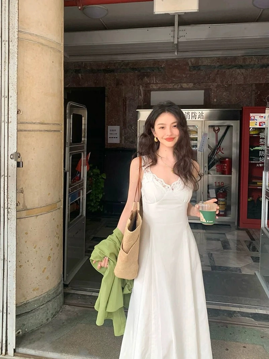 White lace trim V-neck A-line maxi dress shown from the side with straw shoulder bag and green coat
