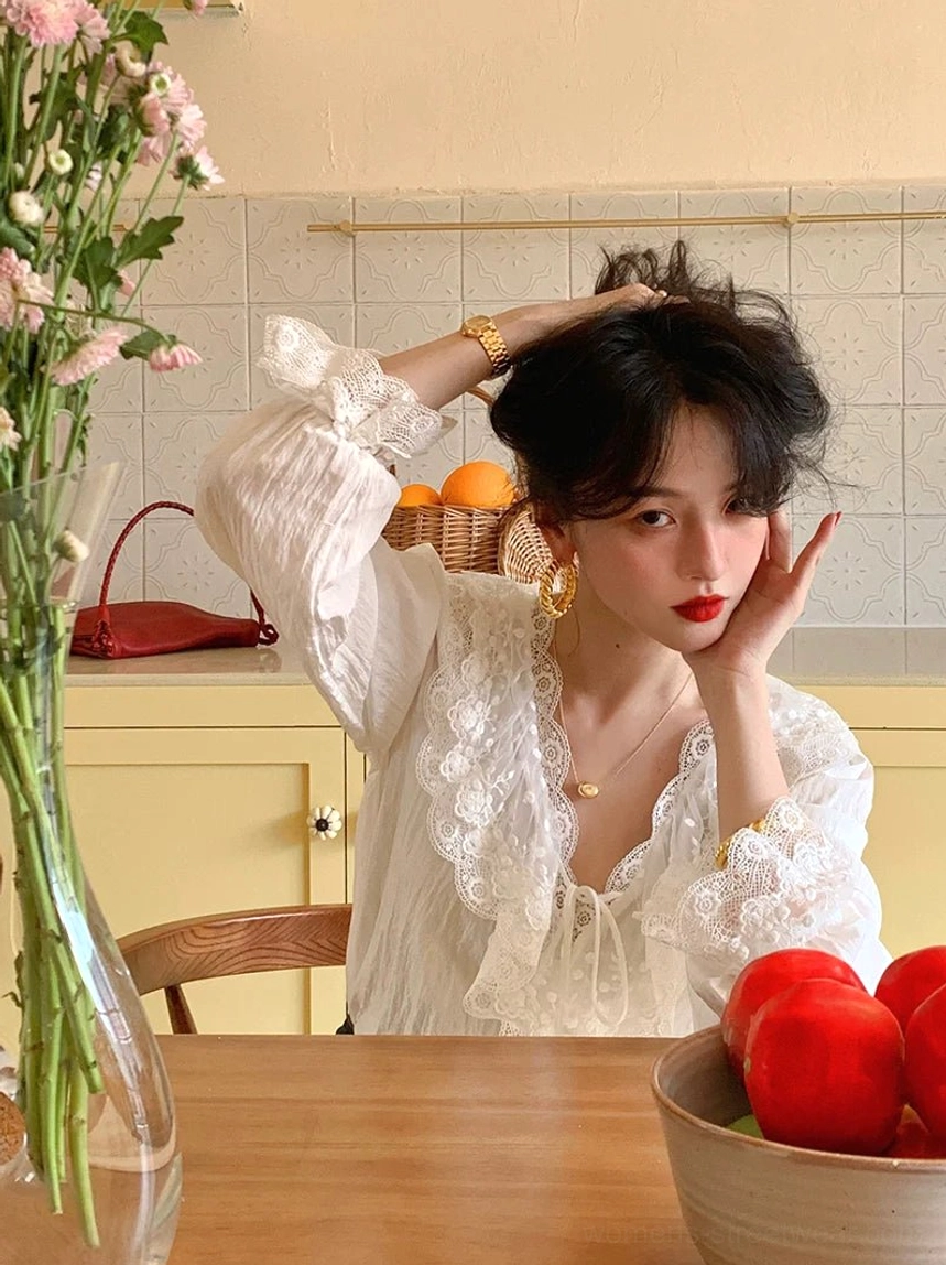 Close-up of white lace-trimmed ruffle blouse with front tie neckline and delicate cuffs styled with gold jewelry in a vintage setting