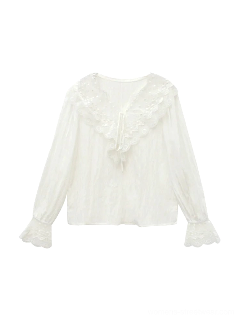 Flat lay of white lace-trimmed ruffled long-sleeve blouse with V-neck front tie, flared lace cuffs, and textured fabric