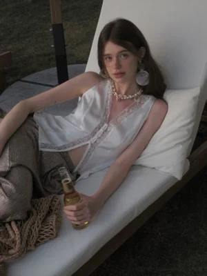 White lace-trimmed V-neck inner vest with front buttons and fitted silhouette styled with metallic wide-leg pants in an outdoor lounge setting