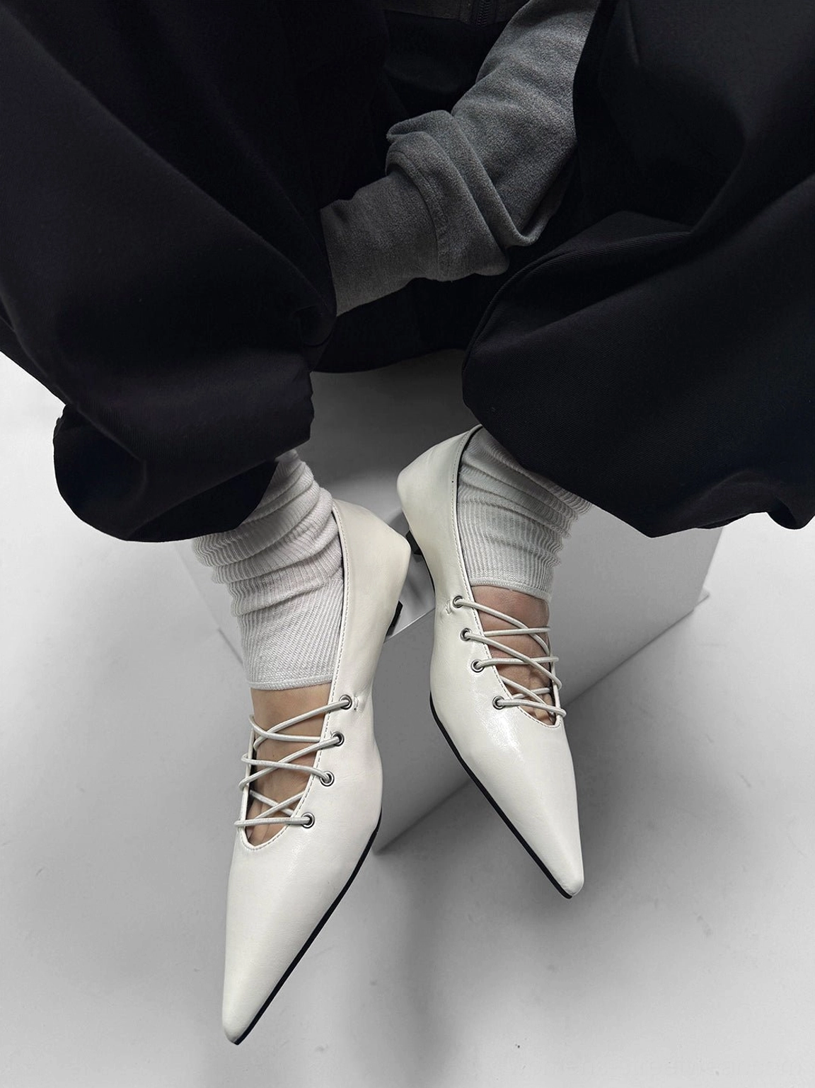 Close-up of white lace-up pointed ballet flats with neat crisscross instep lacing, glossy finish, and streamlined toe shape