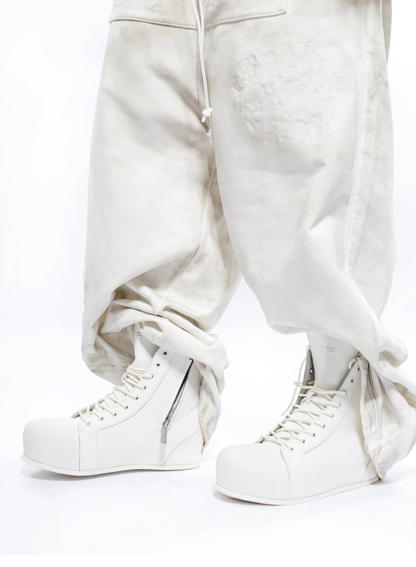 Side rear view of white leather high-top boots with ankle zipper worn with rolled baggy trousers