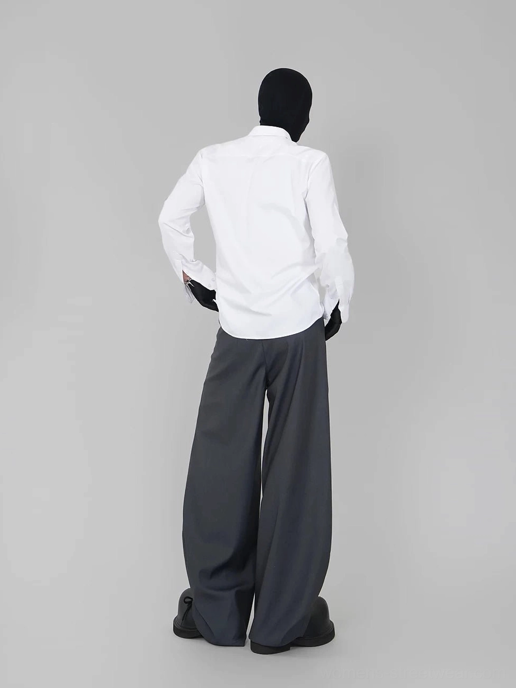 Back view of a white long-sleeve point-collar shirt styled with oversized dark gray wide-leg trousers and black gloves
