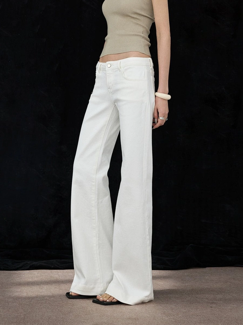 White low-rise flare denim pants shown from the side with long clean legs and classic jean hardware