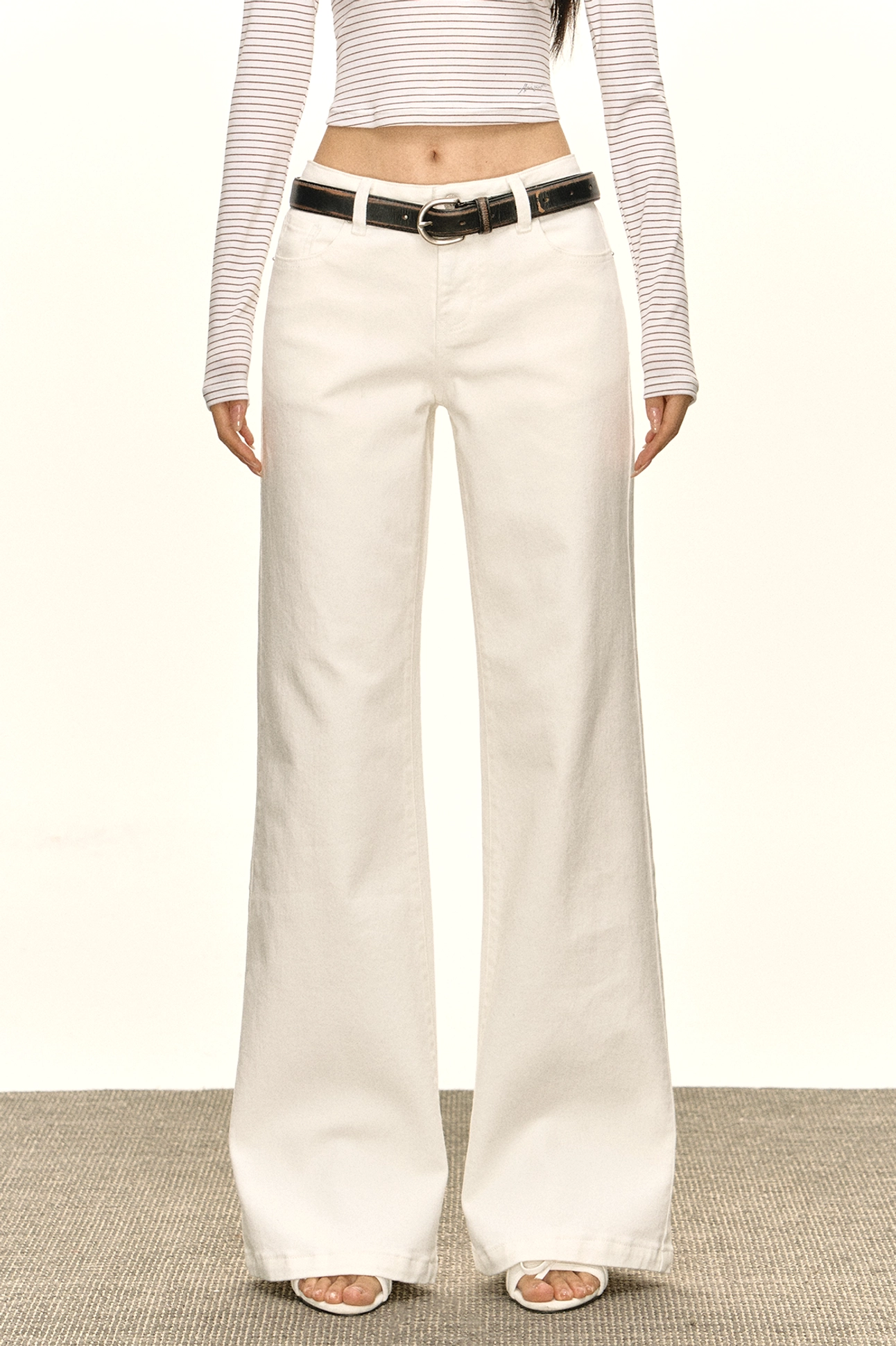 Front view of white low-rise wide-leg jeans styled with a striped cropped top and black belt for a Y2K streetwear outfit