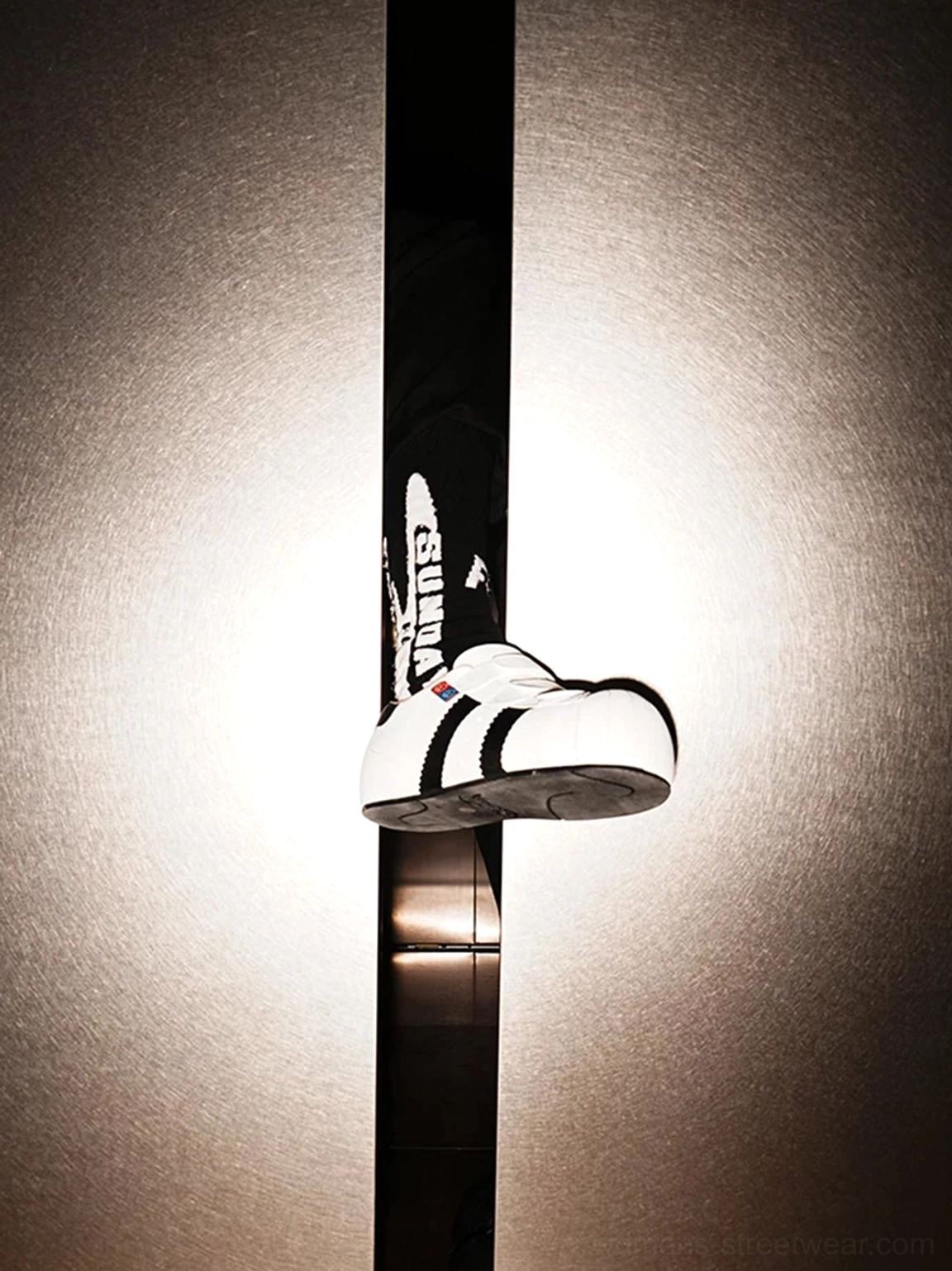 White low-top shell toe sneakers with adjustable straps and black side stripe displayed in a spotlight setting