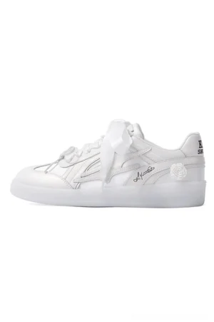 Side profile of a white low-top streetwear sneaker with satin ribbon laces, side stripe detailing, printed upper design, heel tab text, and glossy synthetic leather finish