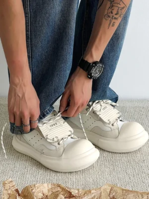 Overhead worn view of white metal stud platform sneakers with twisted two-tone laces, graphic lace tag, and blue denim jeans