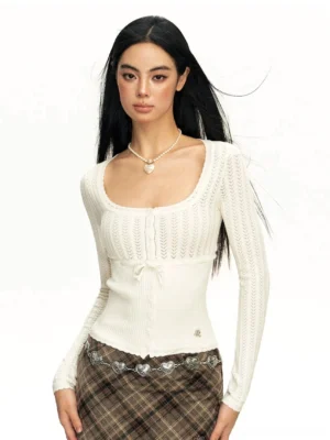 White open-knit ribbed lace cardigan with square neckline, bow-tie front, ruffled hem, and long sleeves styled with a plaid skirt