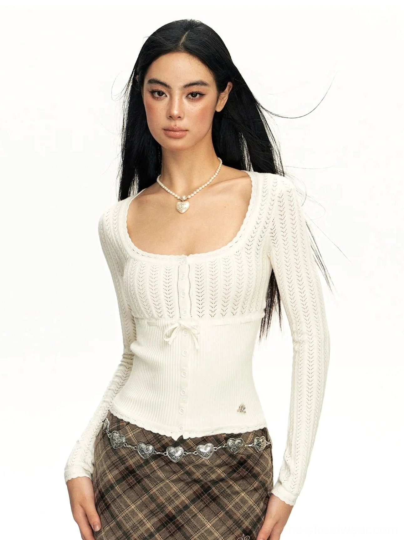 White open-knit ribbed lace cardigan with square neckline, bow-tie front, ruffled hem, and long sleeves styled with a plaid skirt
