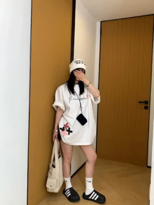 Back view of a woman wearing a loose white oversized cotton floral graphic T-shirt with flower details near the lower hem and casual Seoul streetwear styling