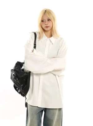 White oversized drop shoulder button down streetwear shirt front view styled with wide leg jeans and black shoulder bag