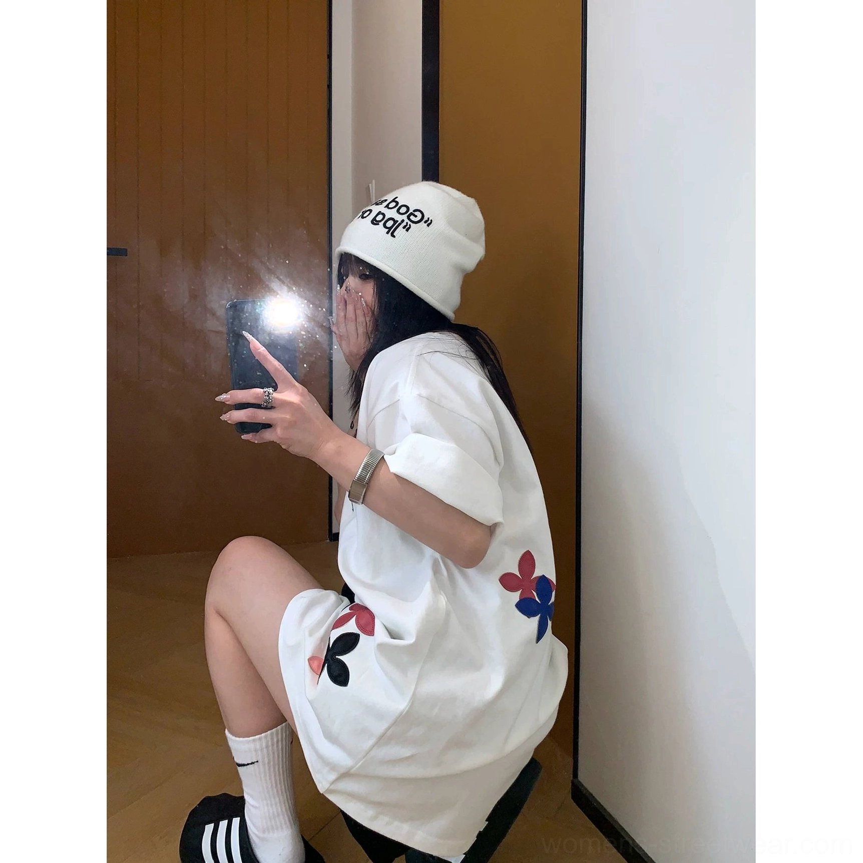Side view of a woman wearing a white oversized floral graphic tee with three-color flower details near the hem and relaxed streetwear accessories